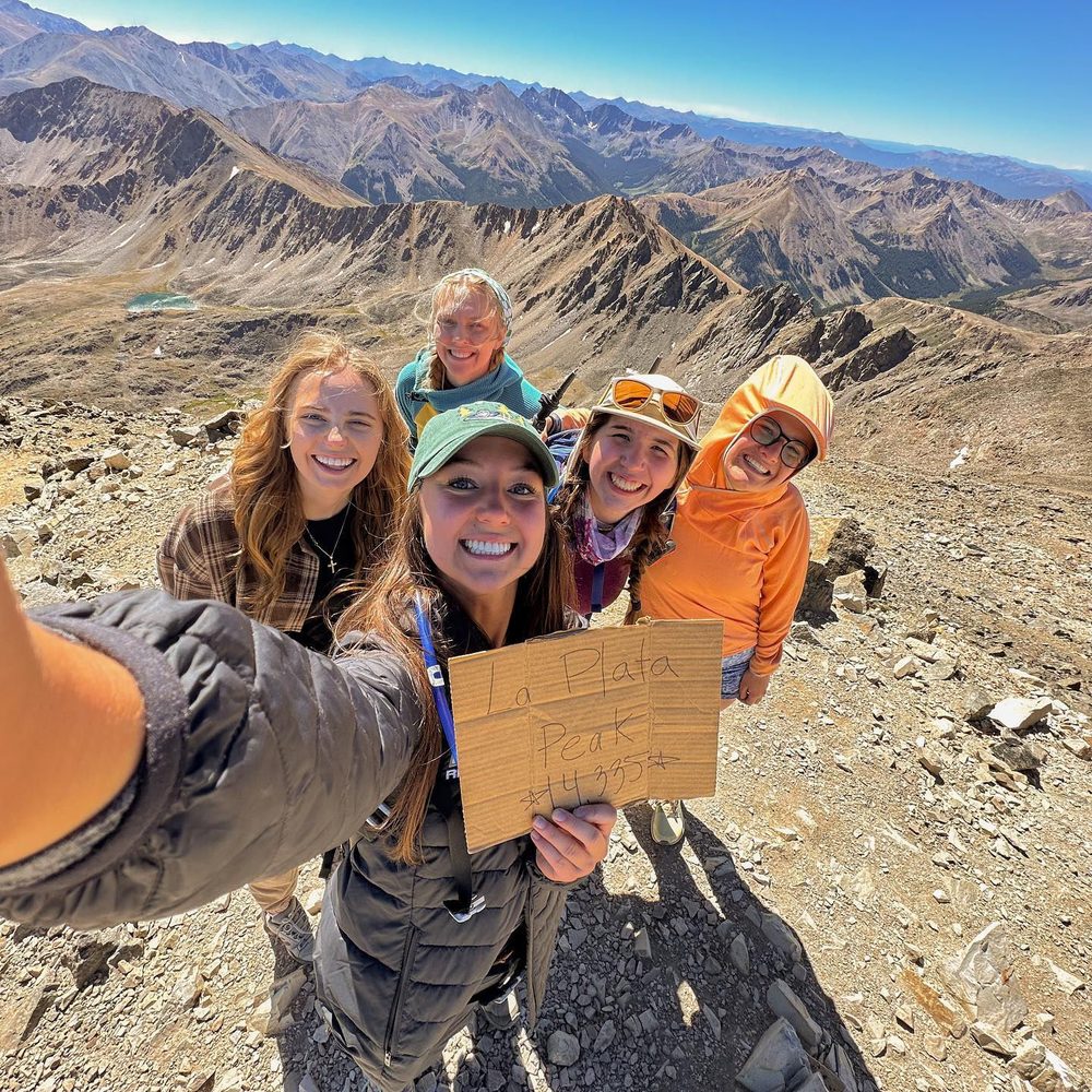 A group of students on a mountain summit holding a sign for La Plata Peak