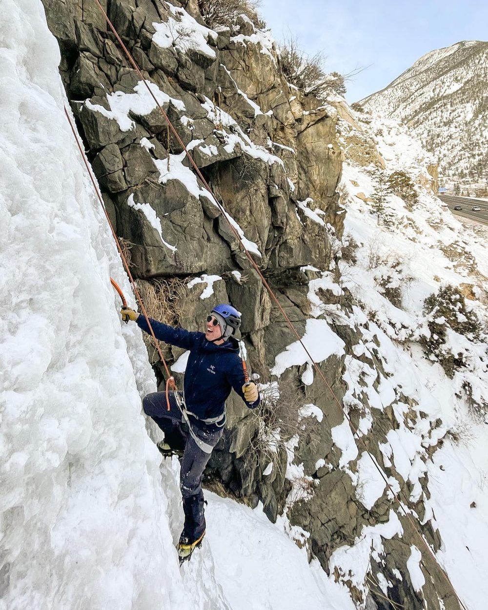 A student ice climbing a frozen waterfall with an ice tool