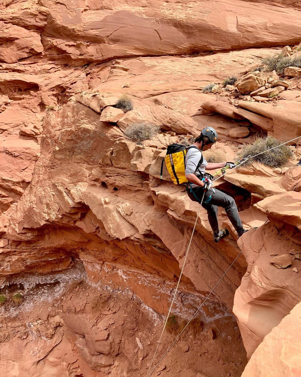 A student rappelling down a red rock slot canyon