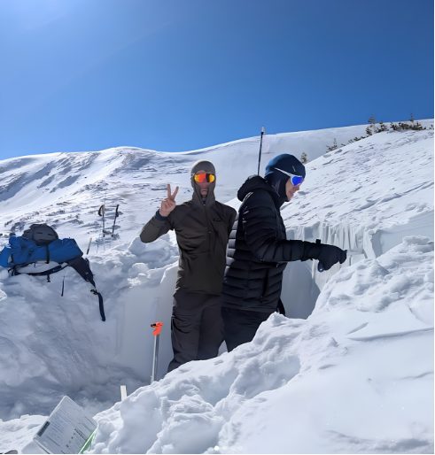 Two students standing in a snow shelter they dug