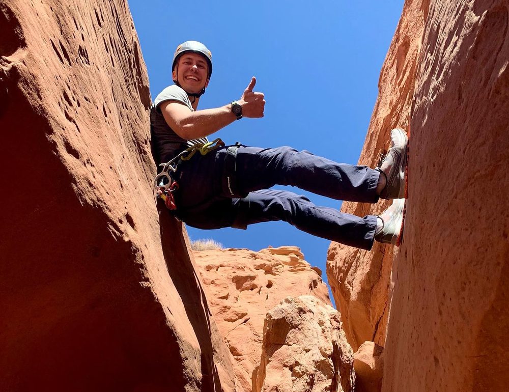 A student rappelling between narrow red rock canyon walls
