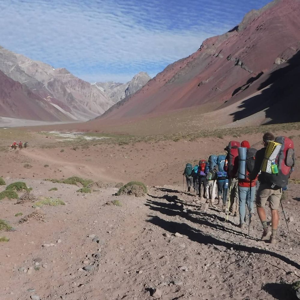 A line of students backpacking through a high desert mountain valley